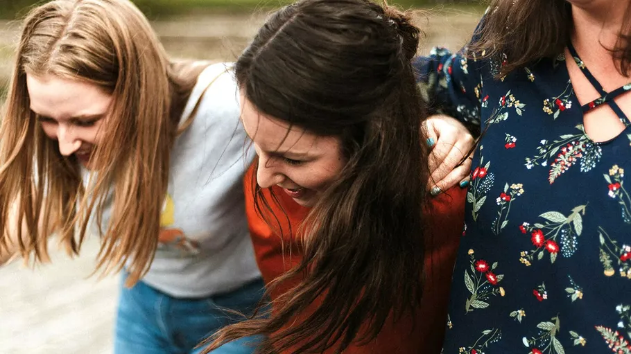 Drei Frauen lachen, Arme um Schultern.