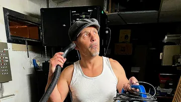 Man holding vacuum hose, looking thoughtful, indoors.