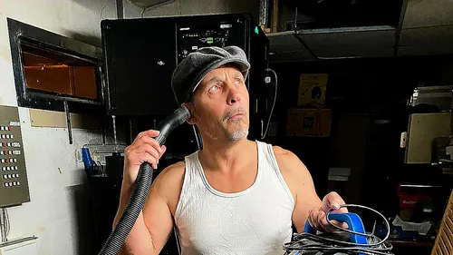 Man holding vacuum hose, looking thoughtful, indoors.