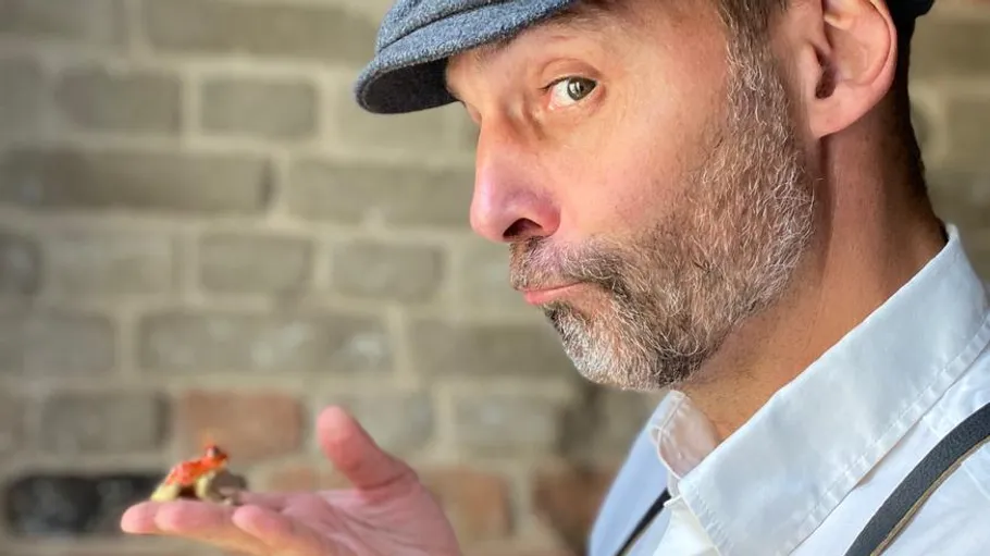 Man holds tiny mushroom sculpture indoors.