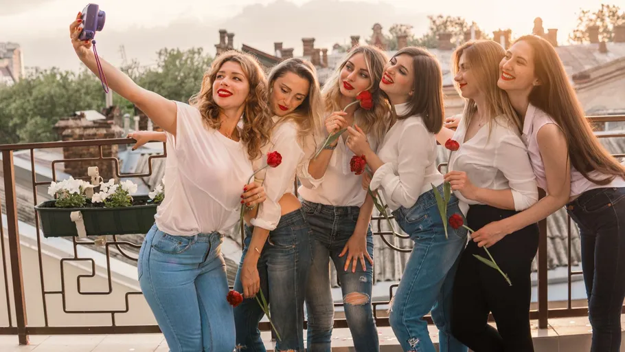 Six women taking selfie with flowers on balcony.