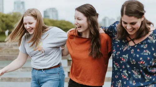 Drei lachende Frauen im Freien, Arm in Arm.