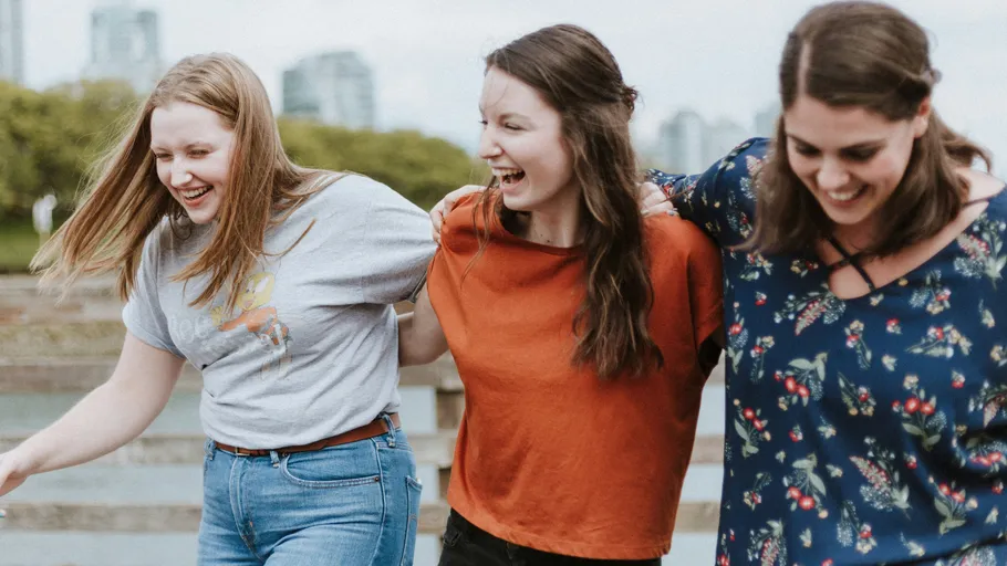 Three women laughing outdoors, arm-in-arm.