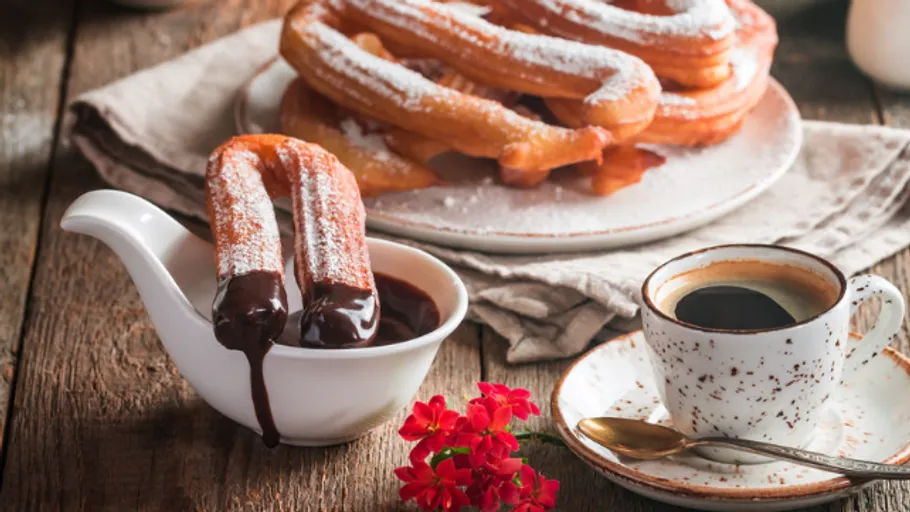 Churros dipped in chocolate beside coffee cup.
