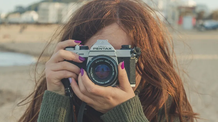 Person holding a camera on a beach.