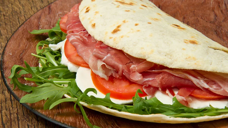 Sandwich mit Schinken, Tomate, Rucola auf Holztisch.