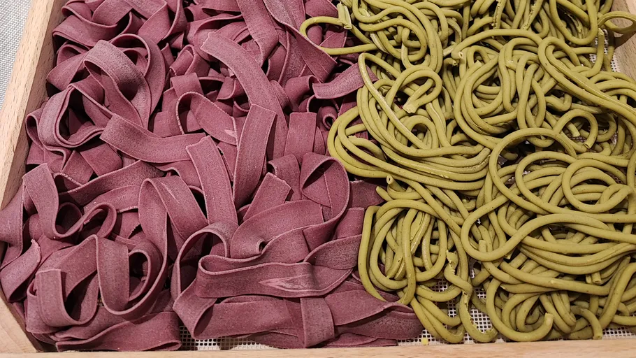 Purple and green pasta in wooden tray.