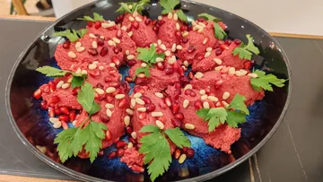 Beet hummus garnished with herbs and seeds.