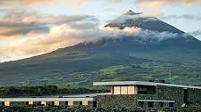 Volcano with clouds above modern building.