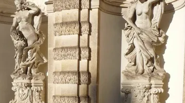 Zwei Steinstatuen in architektonischer Umgebung.