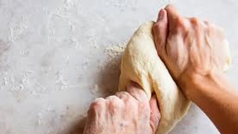 Hands kneading dough on a floured surface.