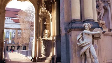 Statue neben verziertem Torbogen, entferntes Gebäude sichtbar.