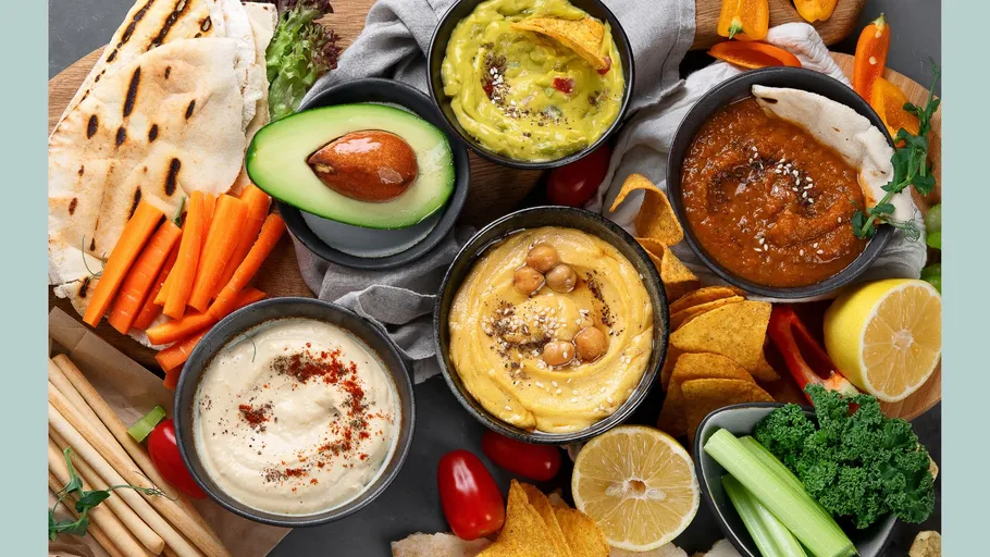 Verschiedene Dips mit Gemüse und Broten präsentiert.