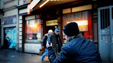Person films couple on street with smartphone.