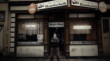 Man stands outside dimly lit bar entrance.
