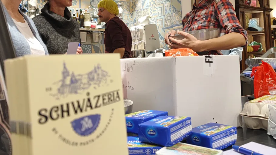 Several people in a deli with cheese and packages.
