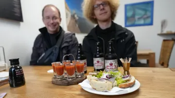 Sandwiches and drinks on table, two people seated.