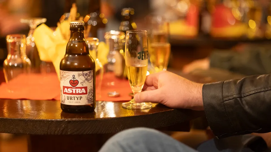 Bierflasche und Hand mit Glas auf Tisch.