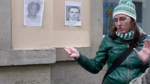 Frau gestikuliert nahe Wand mit zwei Postern.