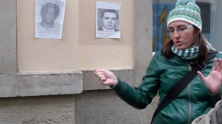 Woman gestures near wall with two posters.
