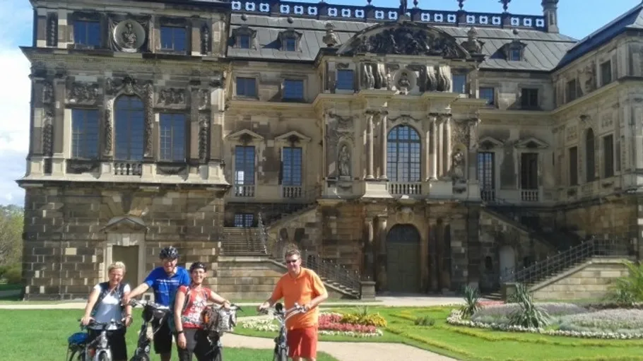 Four people with bikes in front of ornate building.