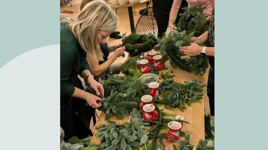 Personen basteln Kränze an Holztisch.