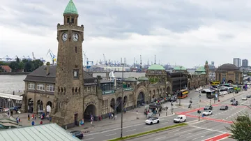 Harbor building with clock tower, cloudy sky.
