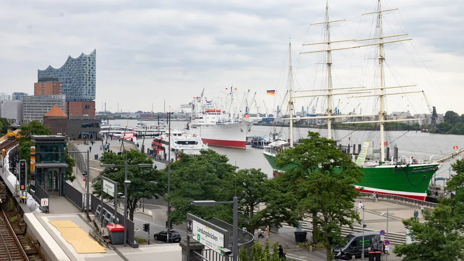 Hafen mit Schiffen, ikonisches Gebäude, bewölkter Himmel.