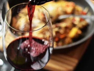 Red wine is poured into a wine glass next to a dish.