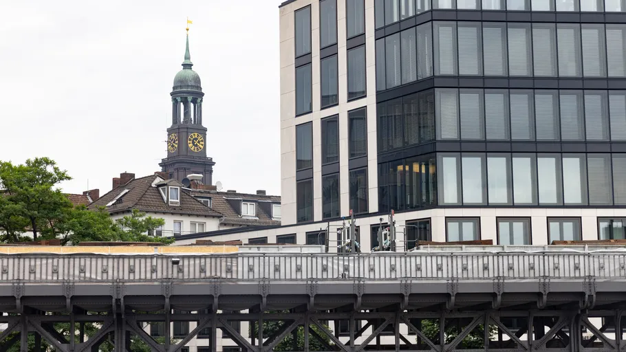 Clock tower and modern building near railway bridge.