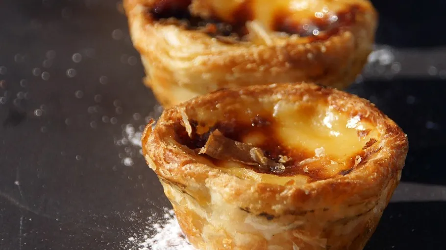 Two custard tarts on a black surface.
