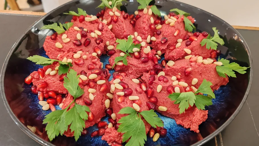 Pink hummus with garnishes on dark plate.