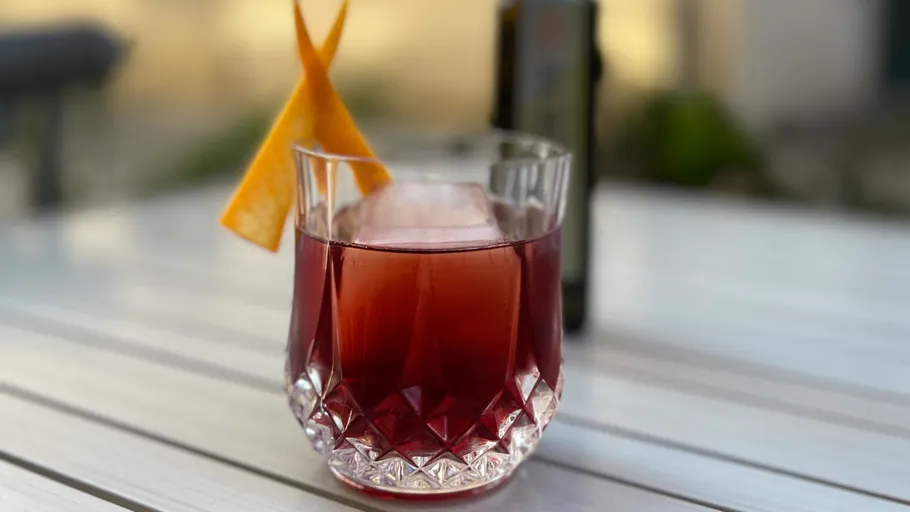 Red cocktail in glass with orange peel garnish.
