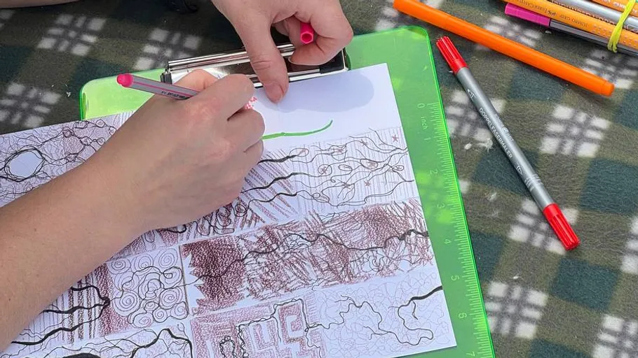 Hands drawing patterns on a clipboard outdoors.