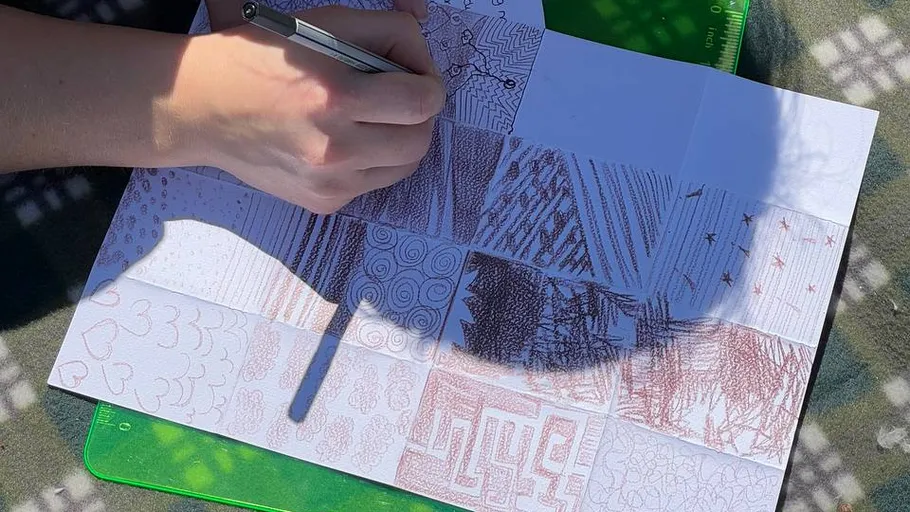 Person zeichnet Muster auf Graphblättern im Freien.