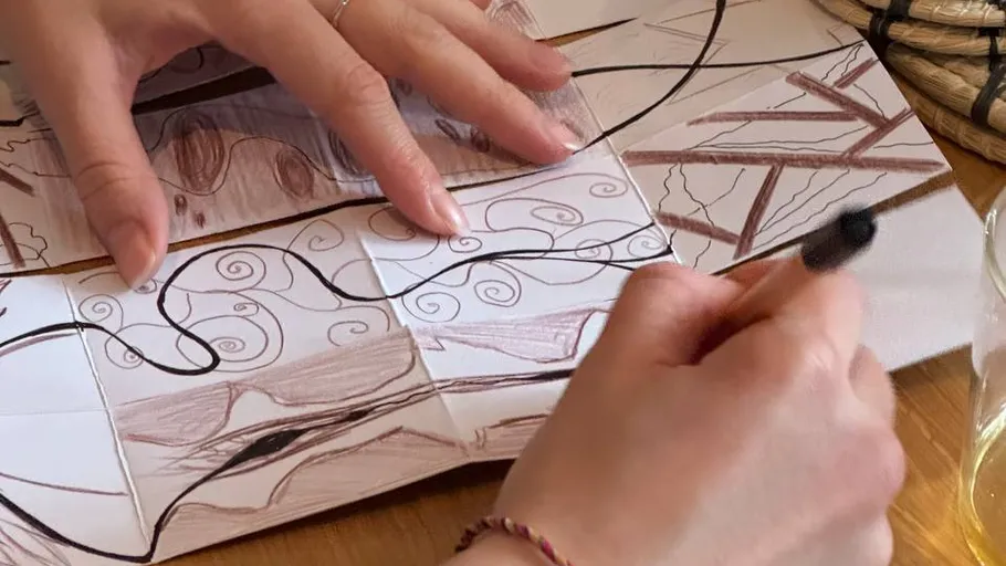 Hände zeichnen auf gefaltetem Papier, Holztisch.