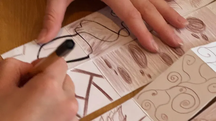 Hands drawing abstract designs on paper.