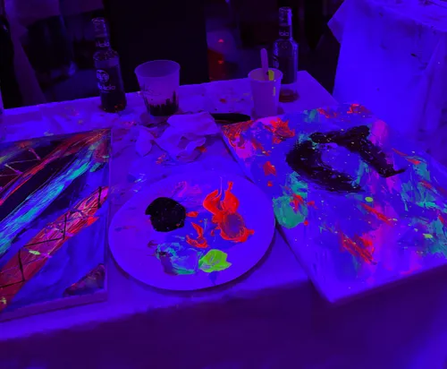 Neon paintings and drinks on table under UV light.