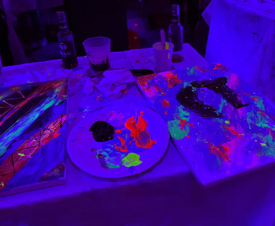 Neonmalereien und Getränke auf Tisch unter UV-Licht.