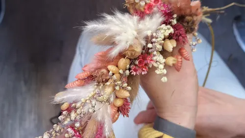 Hand hält bunten Kranz aus Trockenblumen.