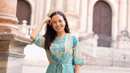 Woman in blue dress, leaning on column outdoors.