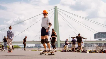 Person skateboarding near bridge, group watching.