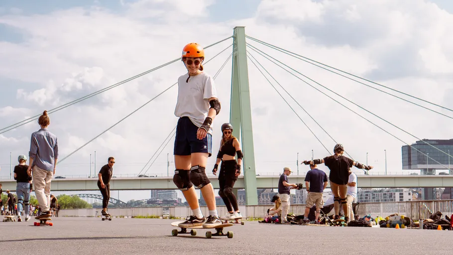 Person skatet nahe Brücke, Gruppe schaut zu.