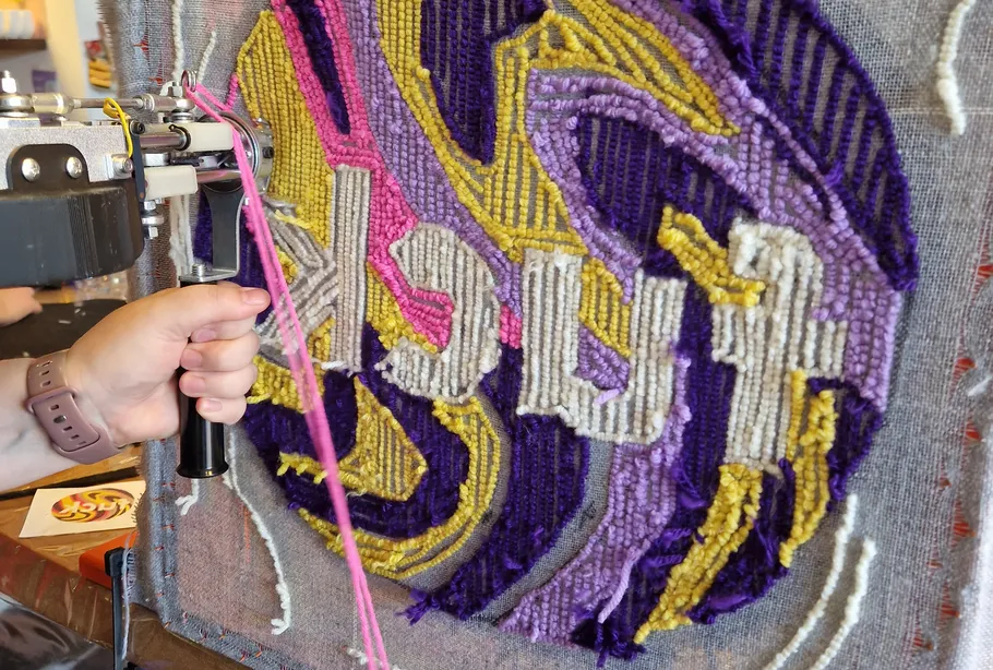 Person tufting colorful design on fabric frame.