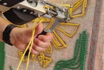 Hand using tufting gun on fabric canvas.