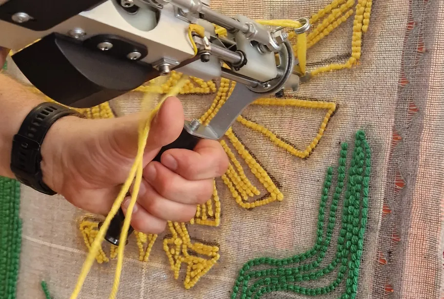 Hand benutzt Tuftpistole auf Stoffleinwand.