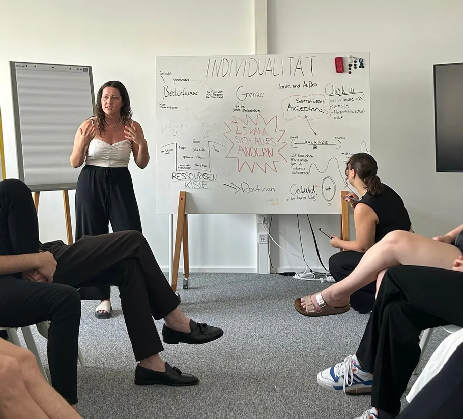 Woman presenting to group with whiteboard notes.
