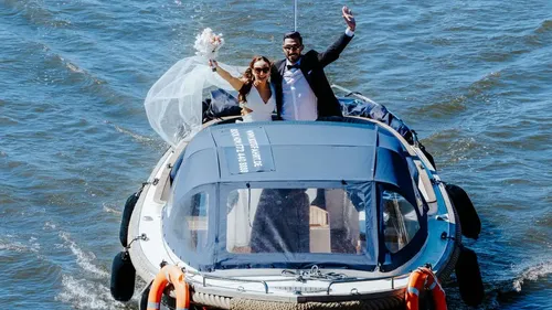 Brautpaar winkt auf Boot im Wasser.