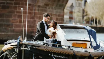 Paar in Hochzeitskleidung umarmt sich auf Boot.