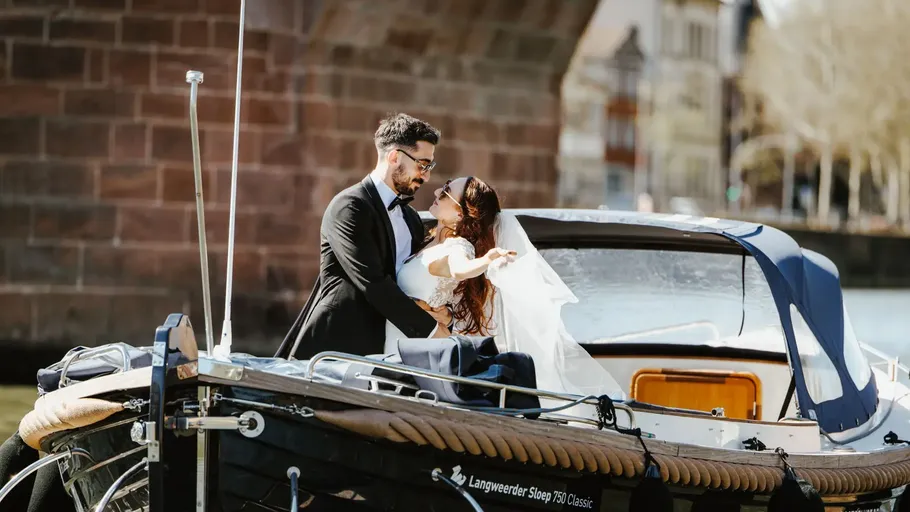 Paar in Hochzeitskleidung umarmt sich auf Boot.